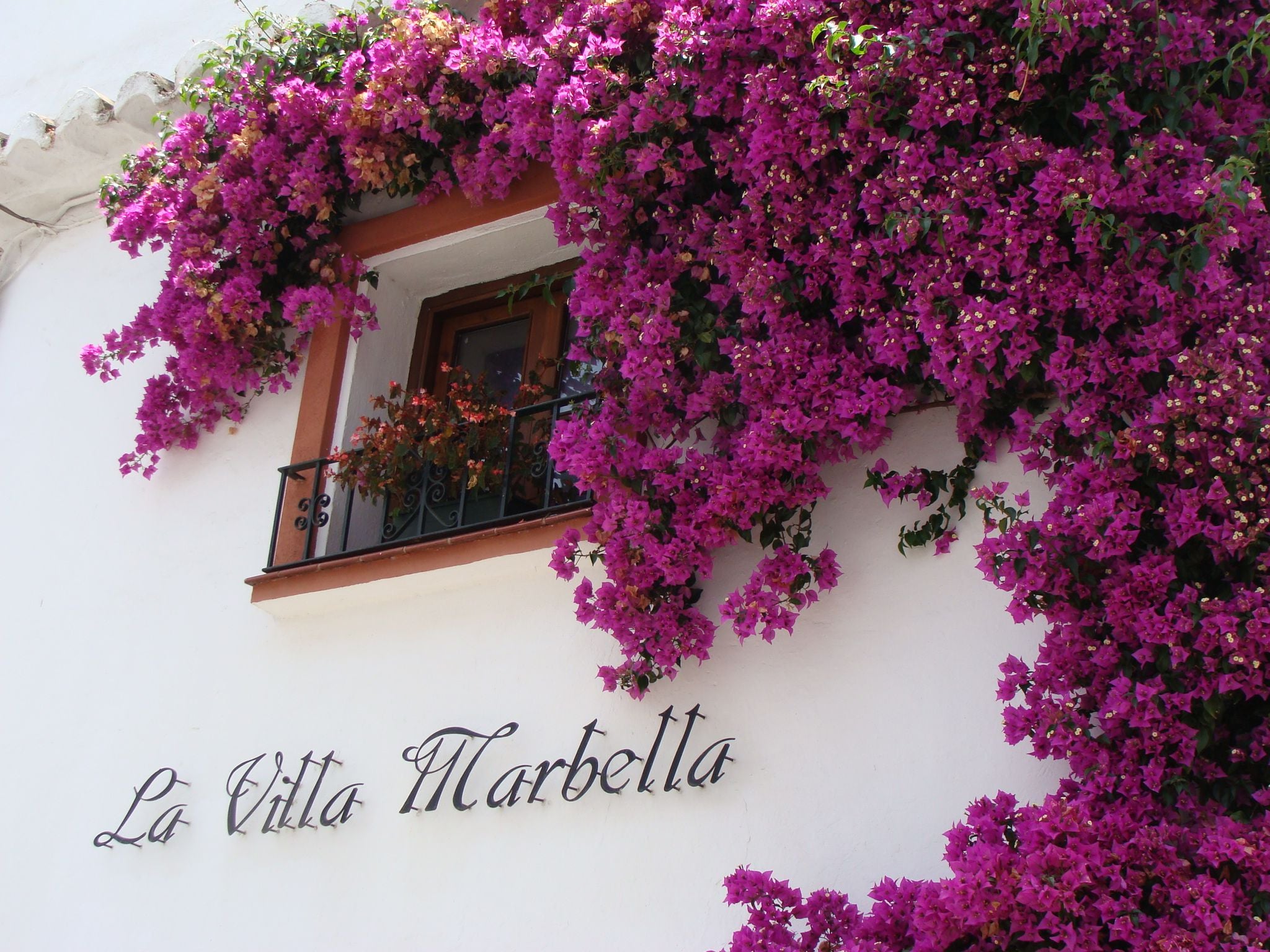 Bougainvillea spilling over the whitewashed facade of La Villa Marbella with the painted wordmark beneath