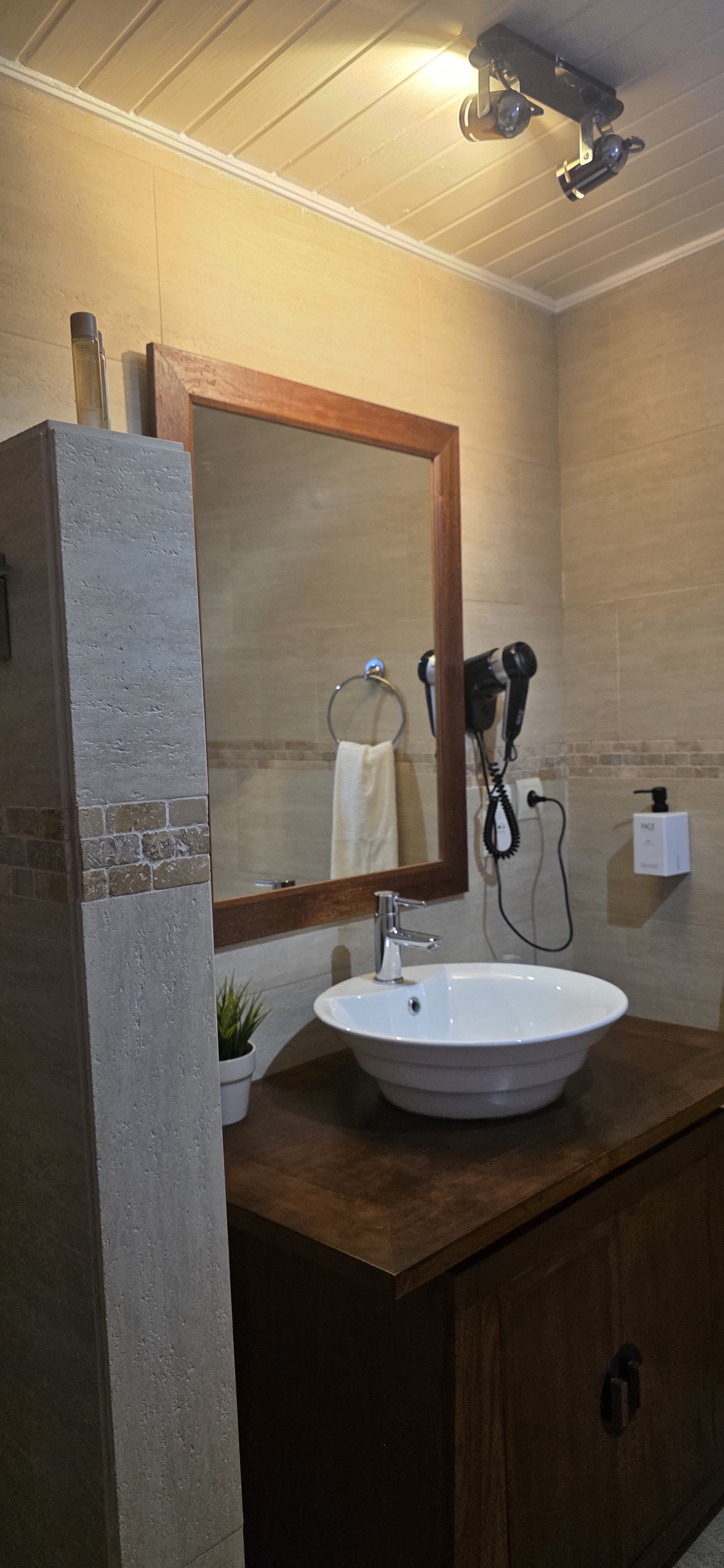A white bowl basin on a dark carved-wood washstand in a stone-tiled bathroom