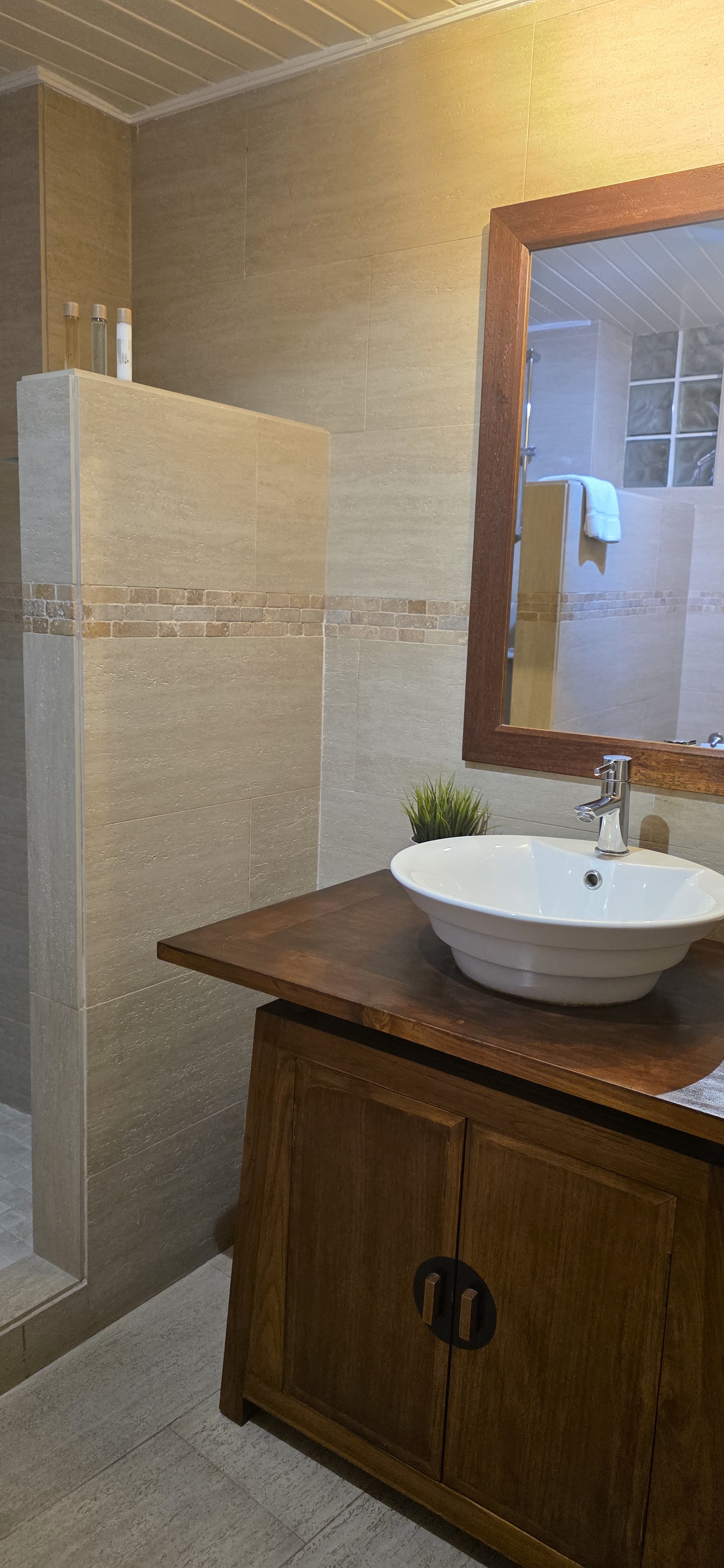 Walk-in shower in warm stone tiles beside a bowl-basin vanity