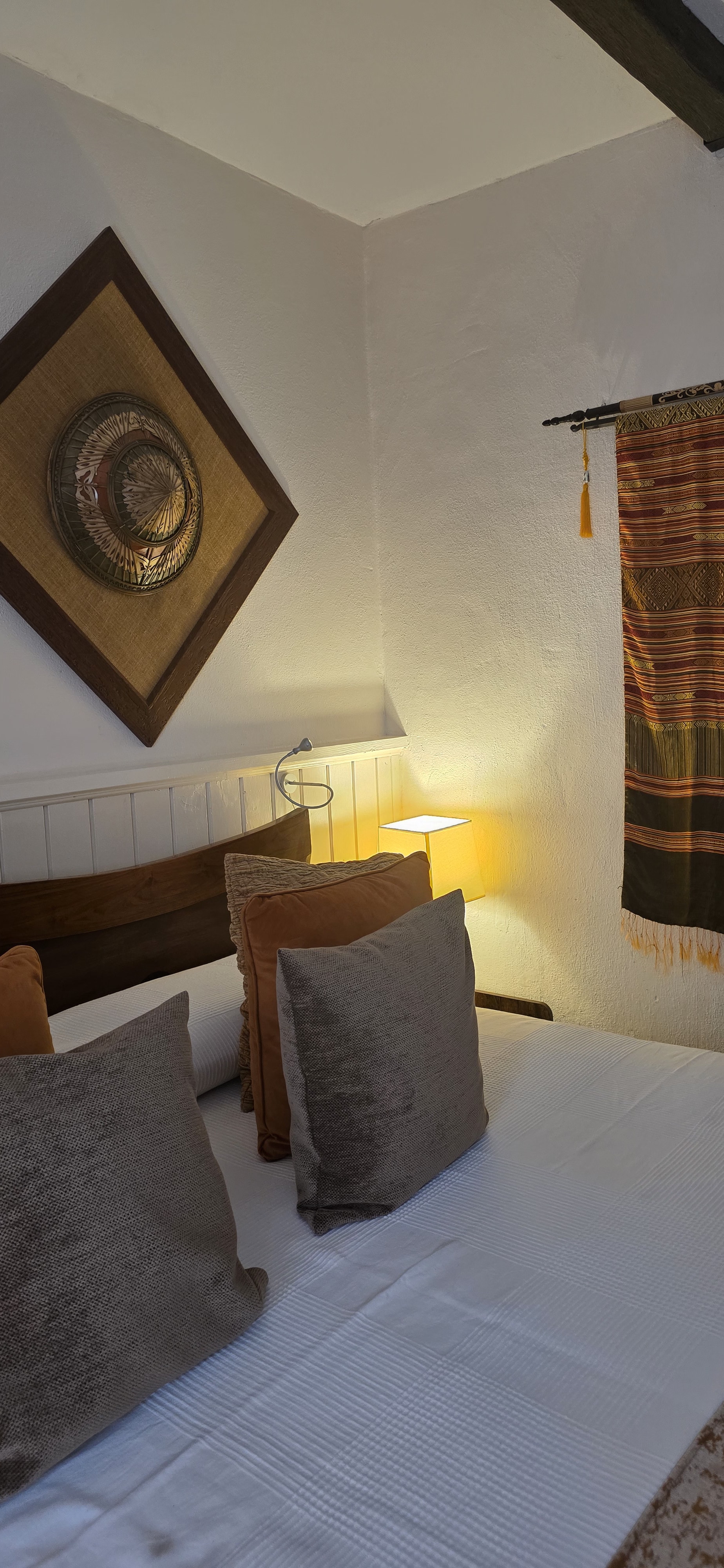 Bedroom corner with woven diamond wall art, textile hanging and layered cushions